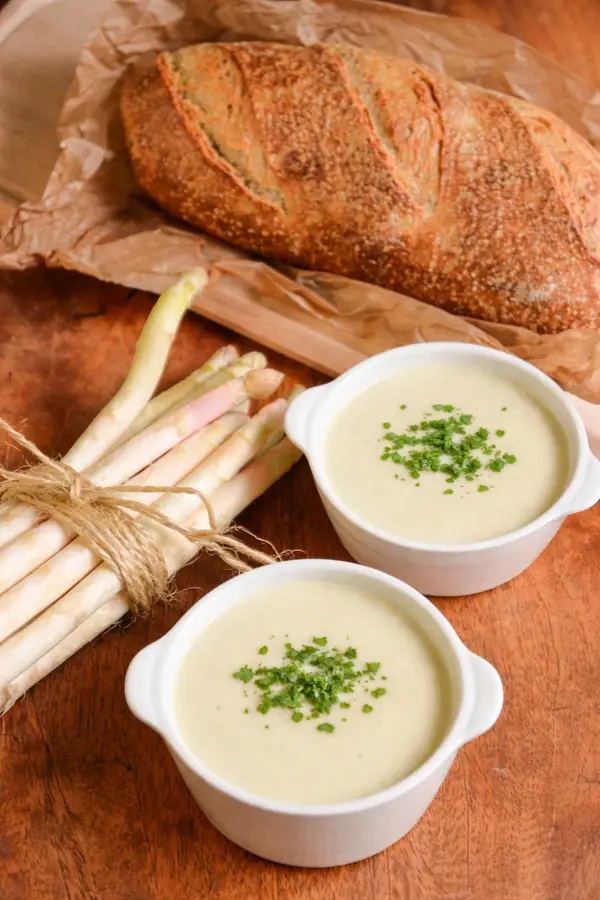 Deux bols de Velouté d'asperges blanches ultra crémeux servis avec du pain de campagne.