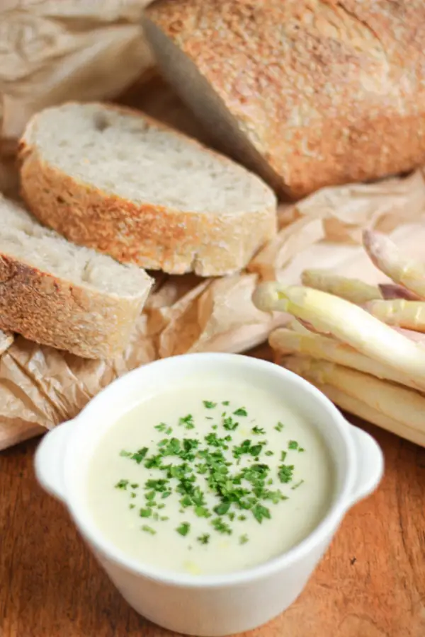 Velouté d'asperges blanches ultra crémeux dans un bol blanc servi avec du pain de campagne.