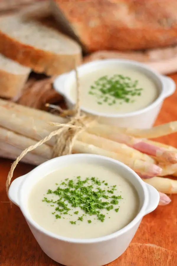 Deux bols de velouté d'asperges blanches ultra crémeux dans un bol blanc servi avec du pain de campagne.
