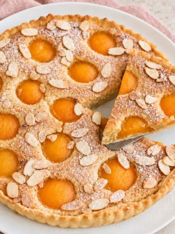 Tarte amandine aux abricots sur assiette blanche.