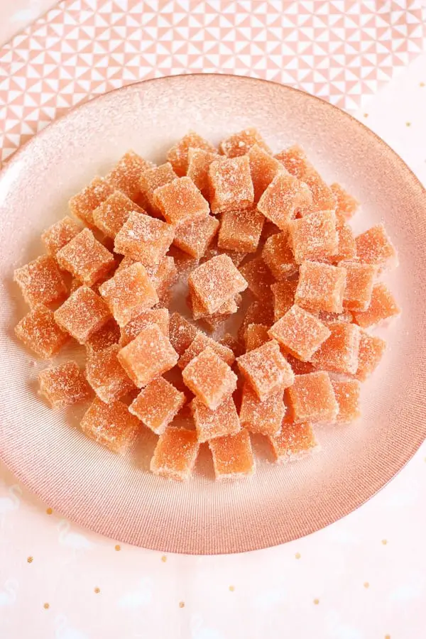 Pâte de coing saupoudrée de sucre cristallisé sur une assiette rose.