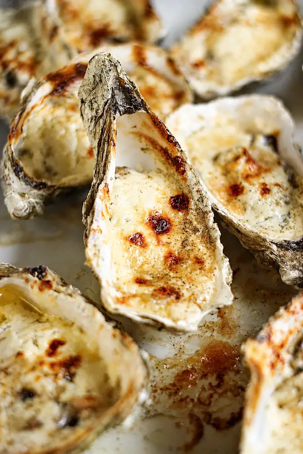 Gros plan sur des huîtres gratinées au four dans leur coquille, avec une garniture crémeuse, fondante et dorée.
