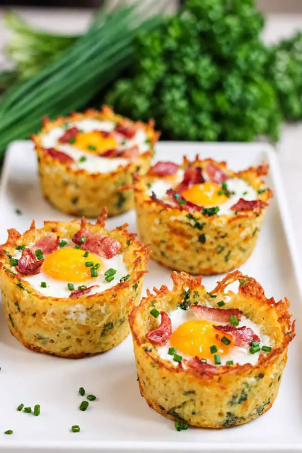 Quatre nids de pommes de terre croustillants garnis d’œufs, de bacon et de ciboulette fraîche