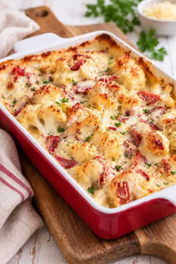 Gratin de chou-fleur au jambon et à la béchamel, doré au four dans un plat rectangulaire rouge, photographié en angle rapproché.