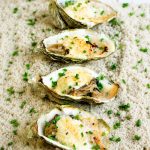 Gros plan sur quatre huîtres gratinées au champagne, crémeuses et dorées, parsemées de ciboulette fraîche.