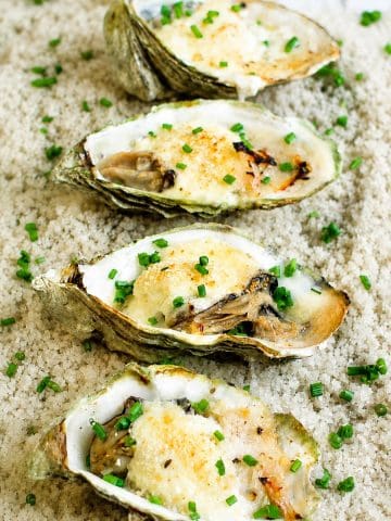 Gros plan sur quatre huîtres gratinées au champagne, crémeuses et dorées, parsemées de ciboulette fraîche.