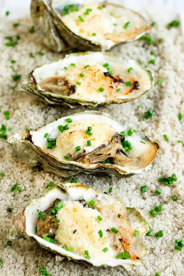 Huîtres gratinées au champagne dans leur coquille, recouvertes d’une garniture crémeuse et parsemées de ciboulette.
