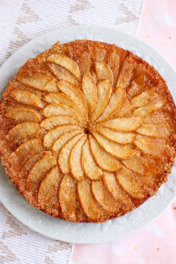 Gâteau moelleux aux pommes caramélisées sur assiette blanche.
