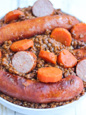 Saucisses aux lentilles avec carottes et saucisses fumées dans un plat blanc.