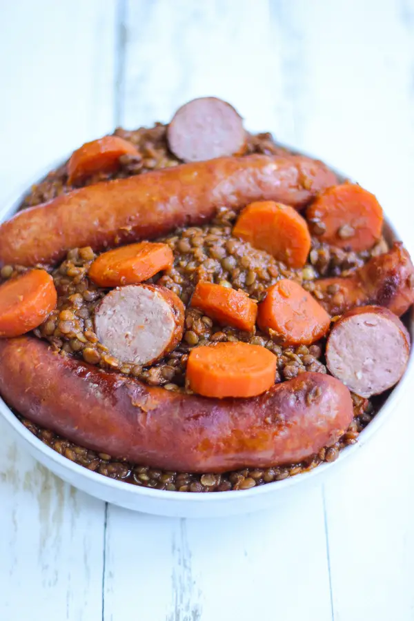 Saucisses aux lentilles avec carottes et saucisses fumées dans un plat blanc.
